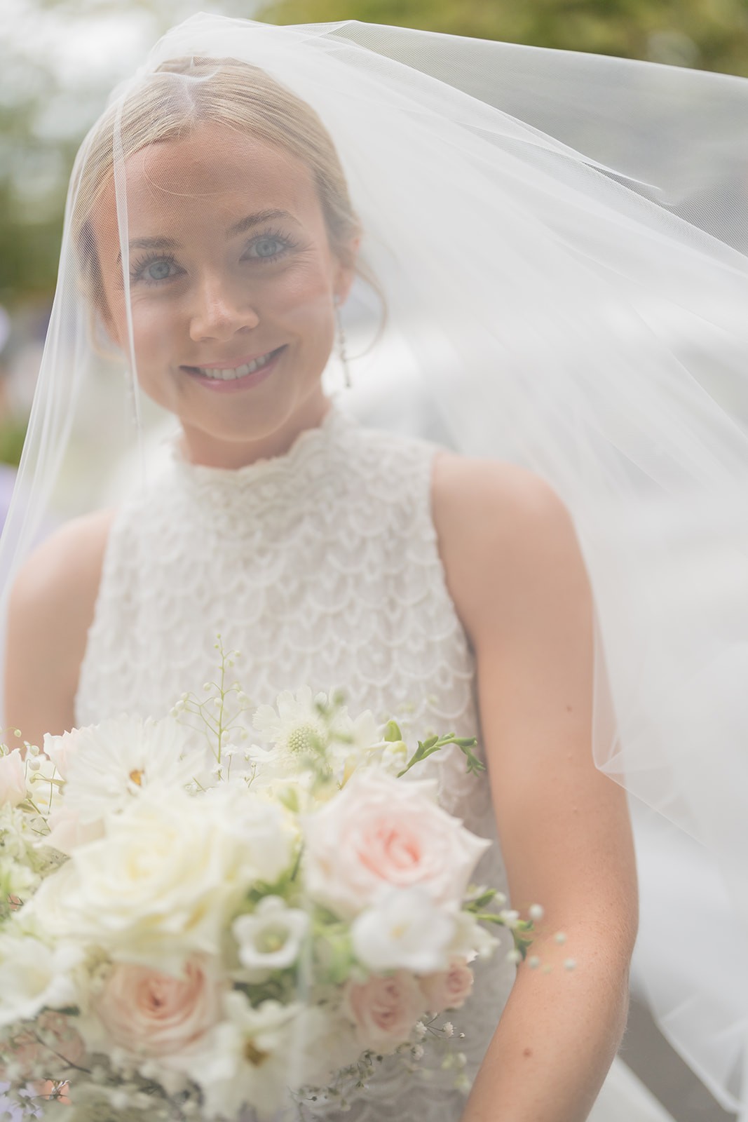Bride smiling beneath her veil with a bouquet of white flowers