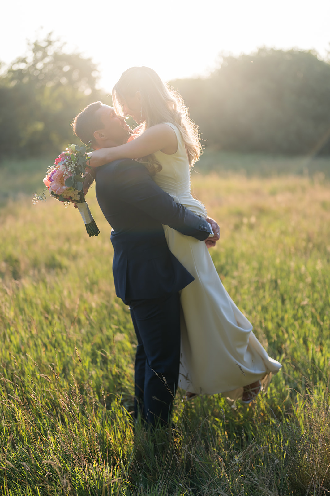 Groom lifting the bride in a sunlit meadow