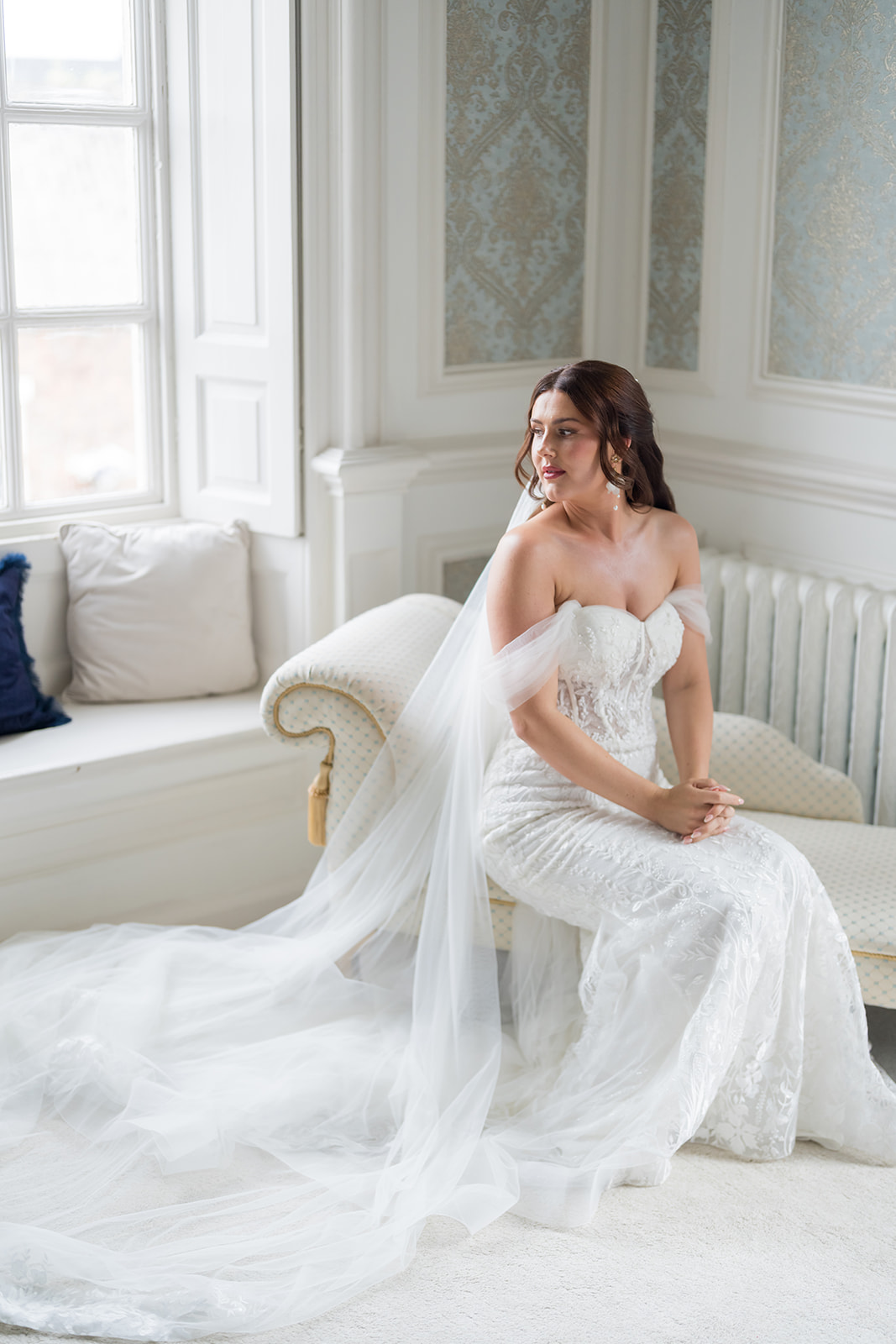 Bride sitting beside a window in her wedding dress