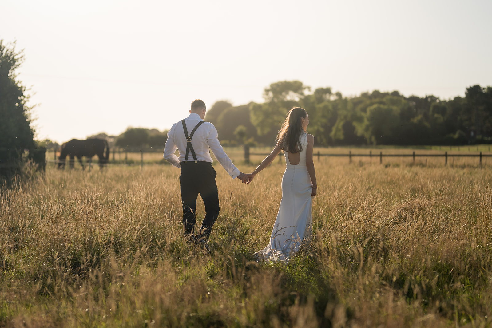 Bride and groom walking hand in hand through long grass