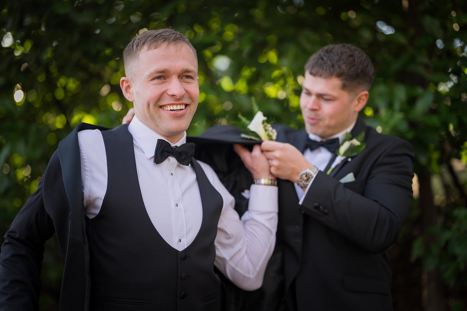 Groom laughing as a friend adjusts his tie