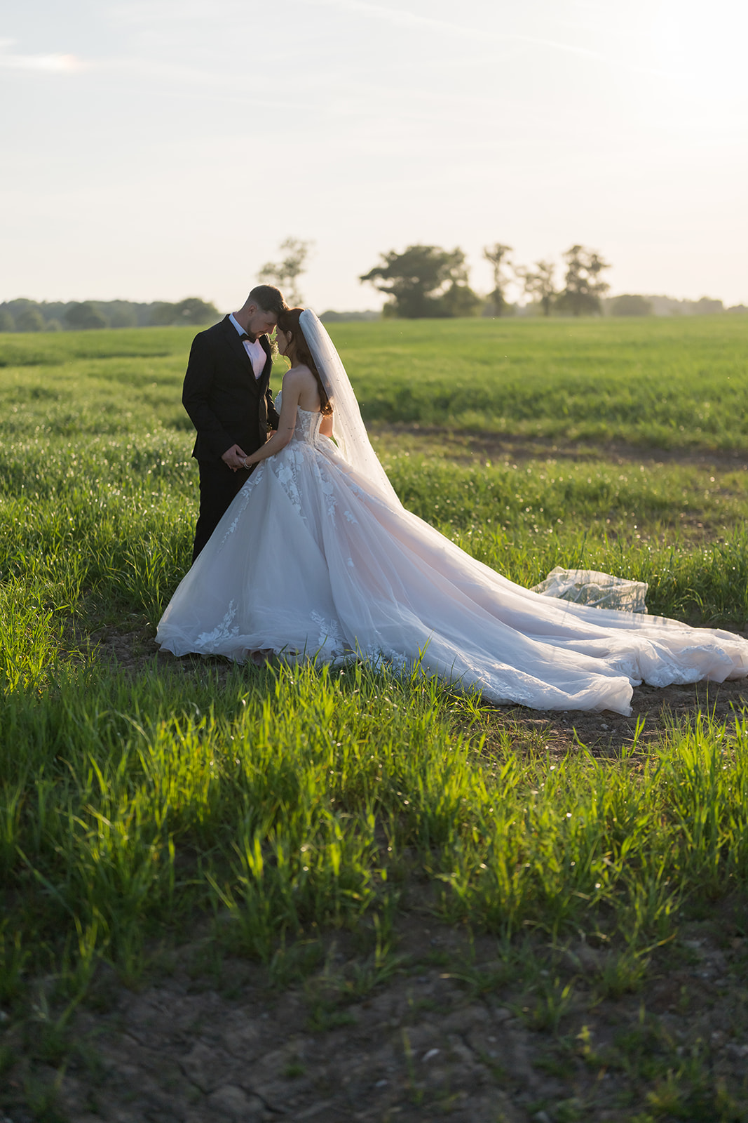 Bride and groom standing together in a sunlit meadow