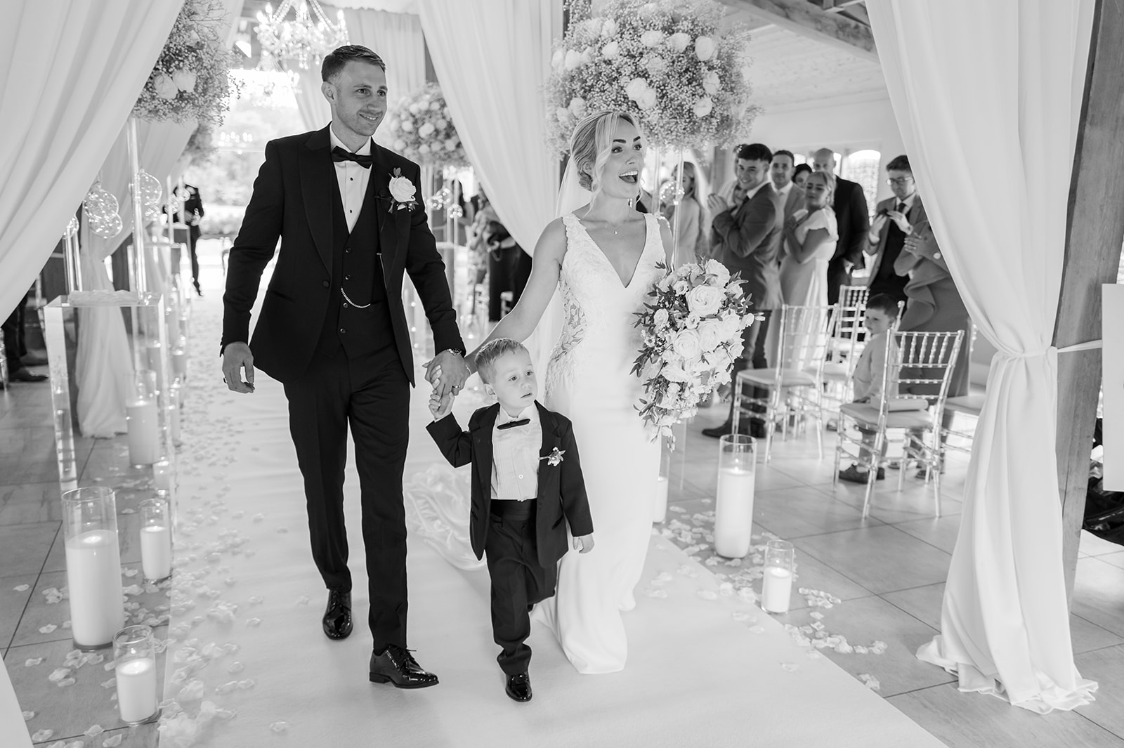Black-and-white photograph of newlyweds beneath a floral ceremony arch