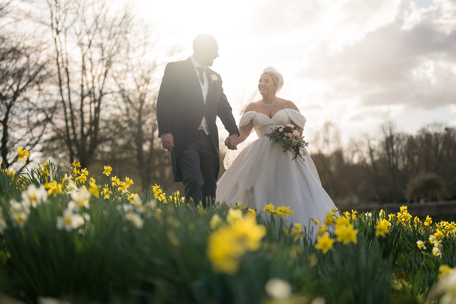 Bride and groom walking among daffodils in low sunlight