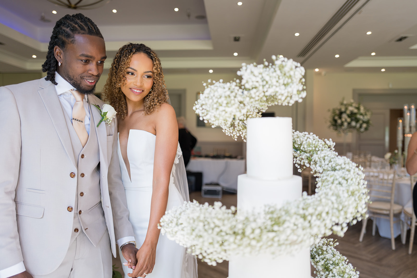 Newlyweds posing beside a tiered wedding cake and white flowers