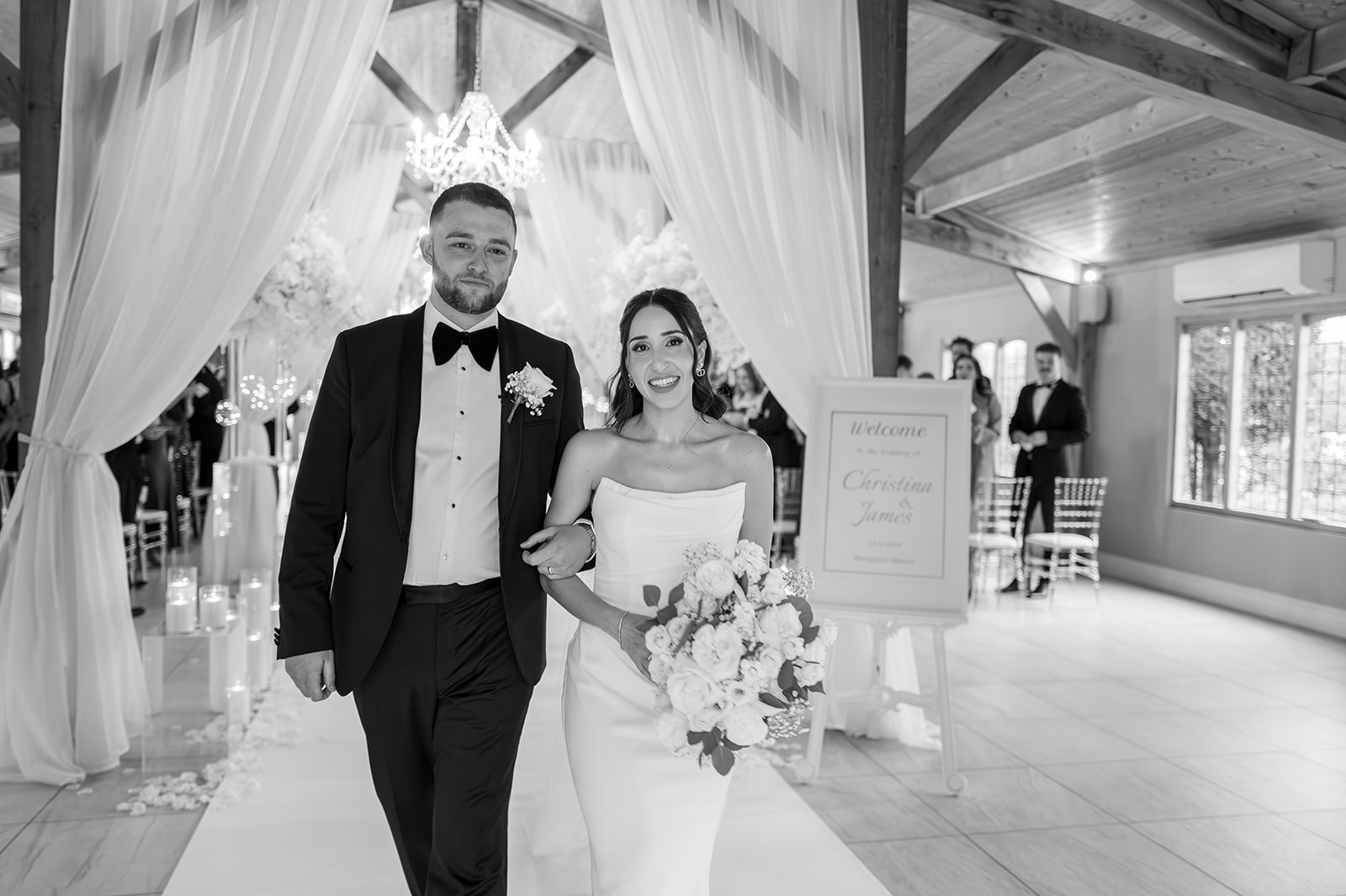 Black-and-white photograph of newlyweds walking through their ceremony room