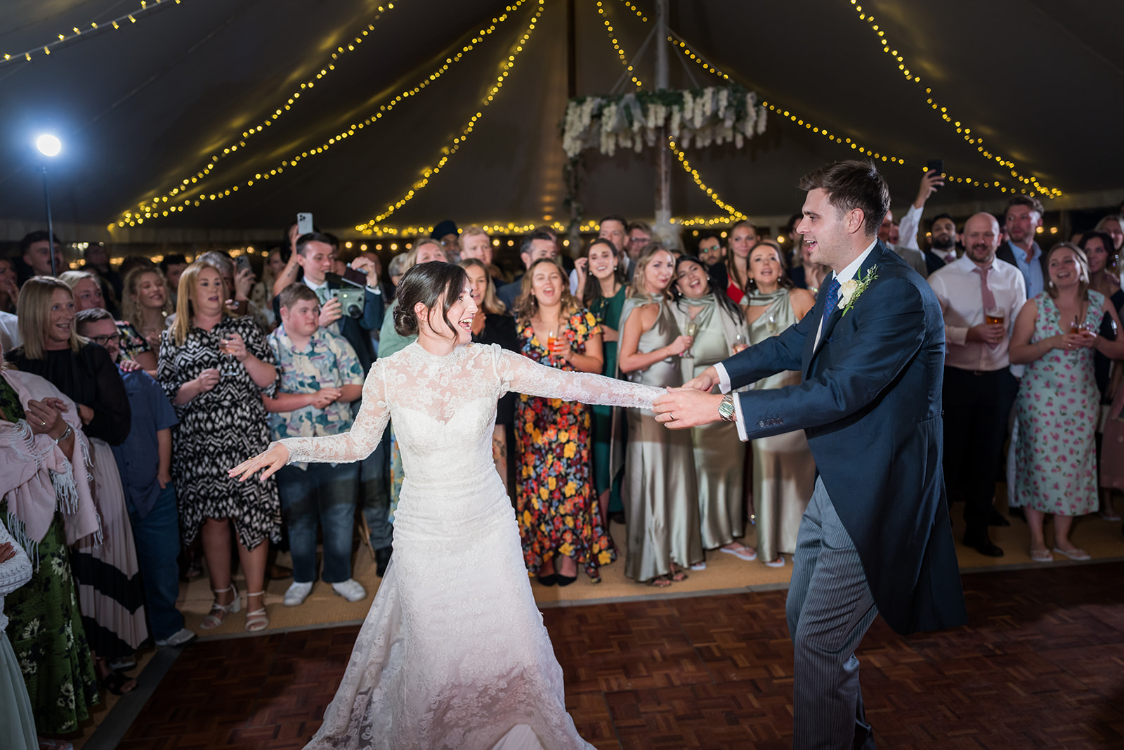 Bride and groom dancing together beneath strings of lights
