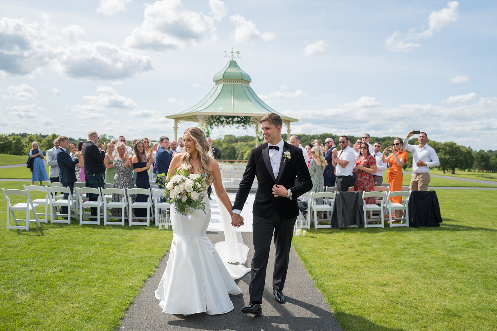 Newlyweds leaving an outdoor ceremony with guests watching