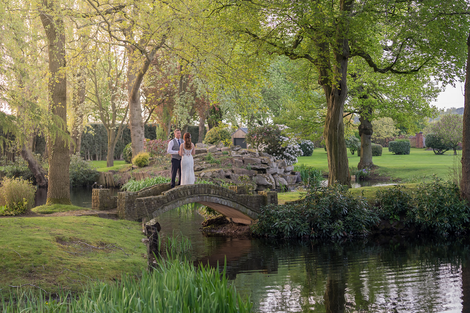 Newlyweds standing on a small stone bridge in a green garden