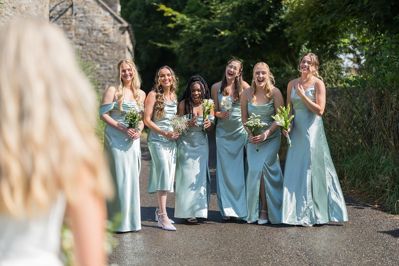 Bridesmaids laughing towards the bride outdoors
