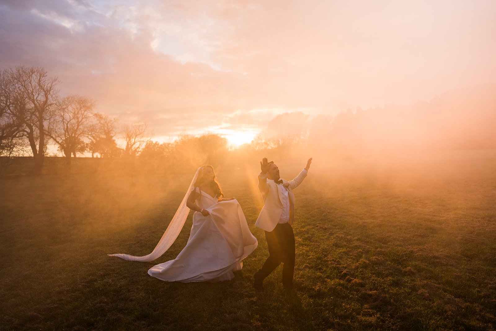 Newlyweds embracing in a field at sunset