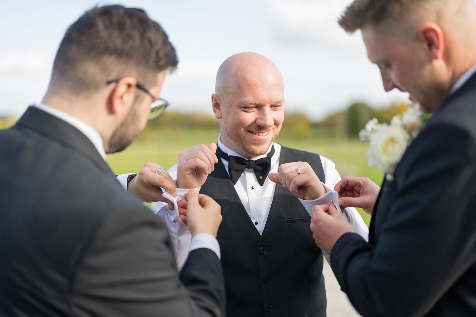 Groom laughing as friends help straighten his tie