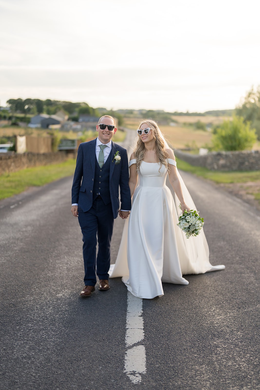 Bride and groom walking hand in hand along a country road